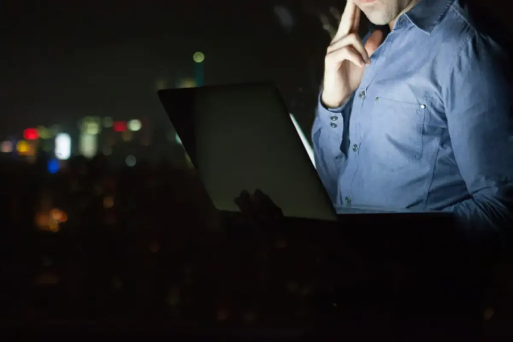 Business professional using a laptop at night with city lights in the background