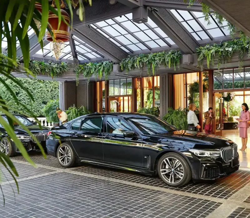 Black BMW serie 5 parked in front of a luxurious hotel with staff welcoming guest.