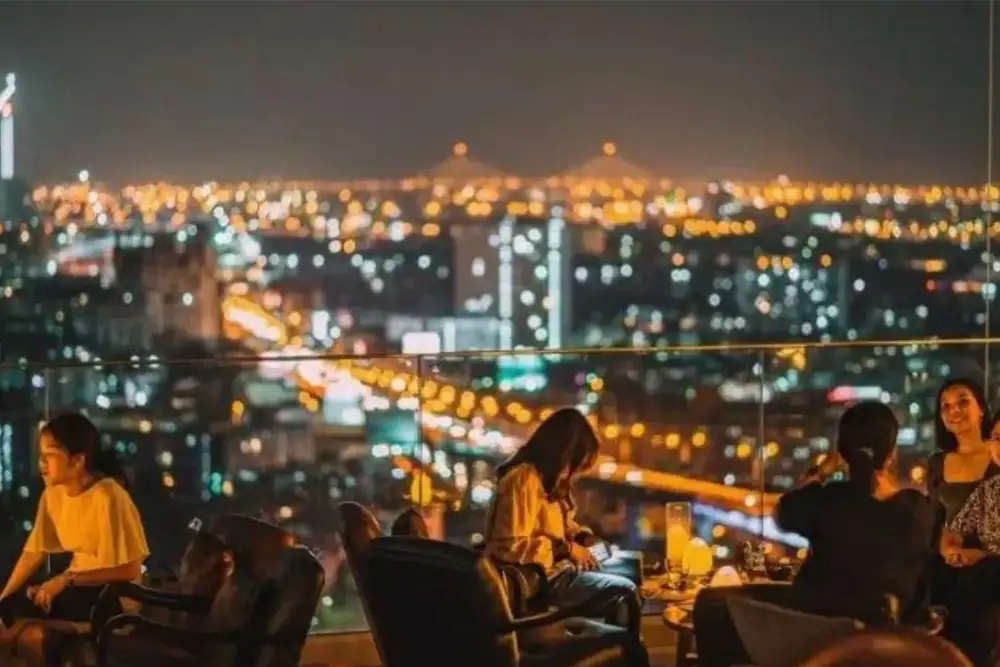 guests seated at a bangkok rooftop bar overlooking the city at night